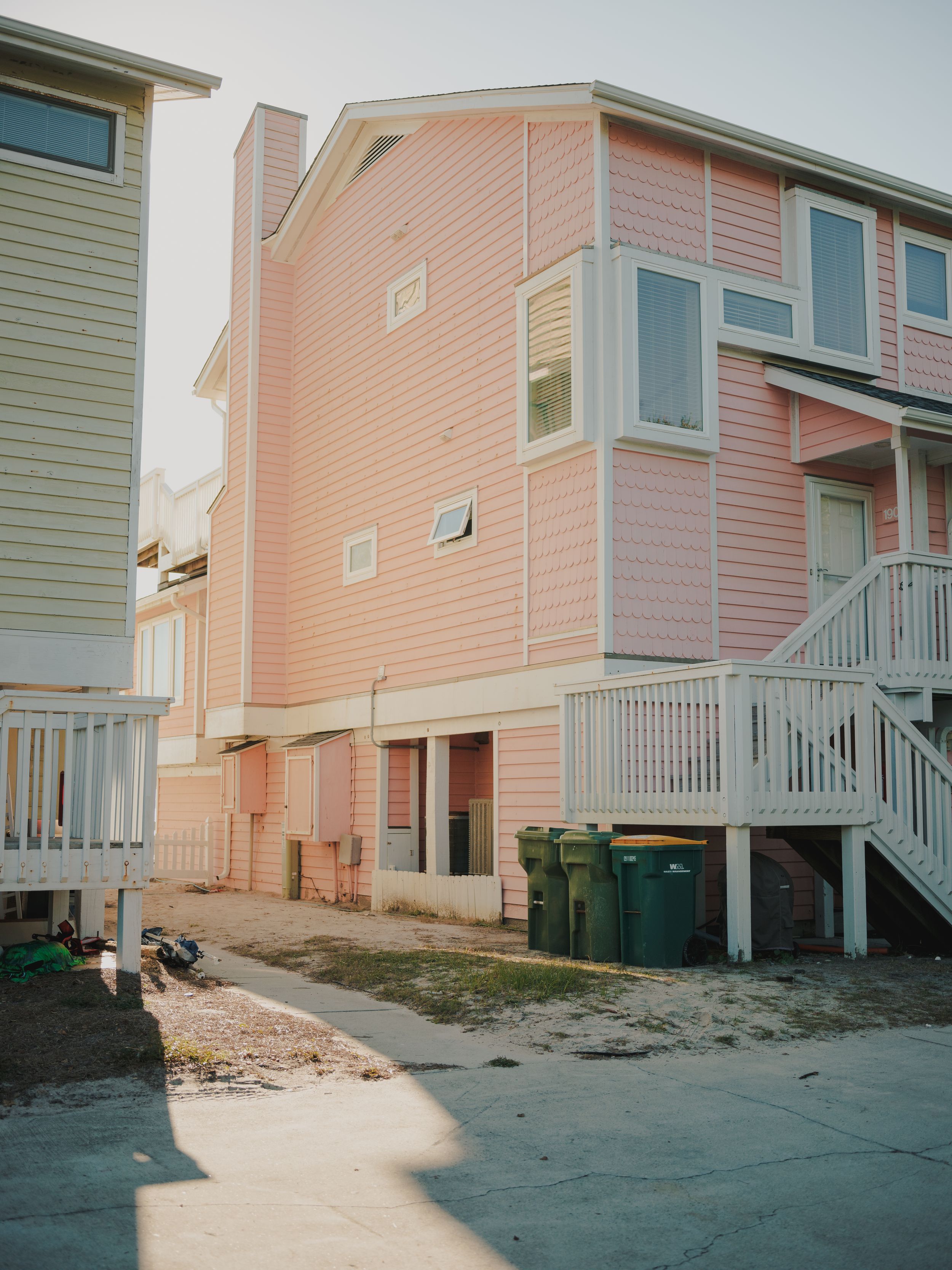 Pink coastal homes on stilts with exterior stairs and sand underneath in a beachfront residential area.