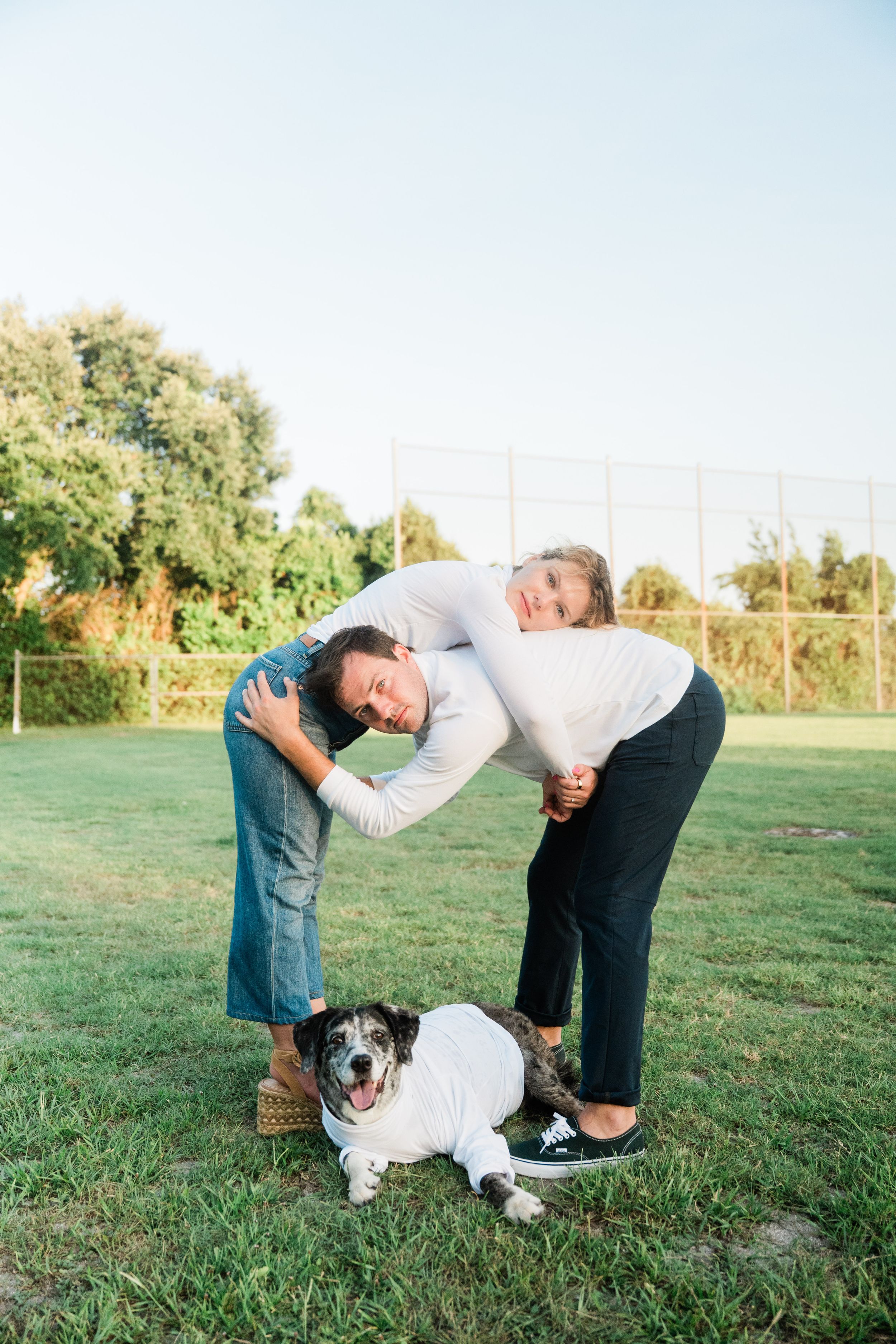 A spotted Australian Shepherd dog plays and interacts with someone on a grassy field at sunset.