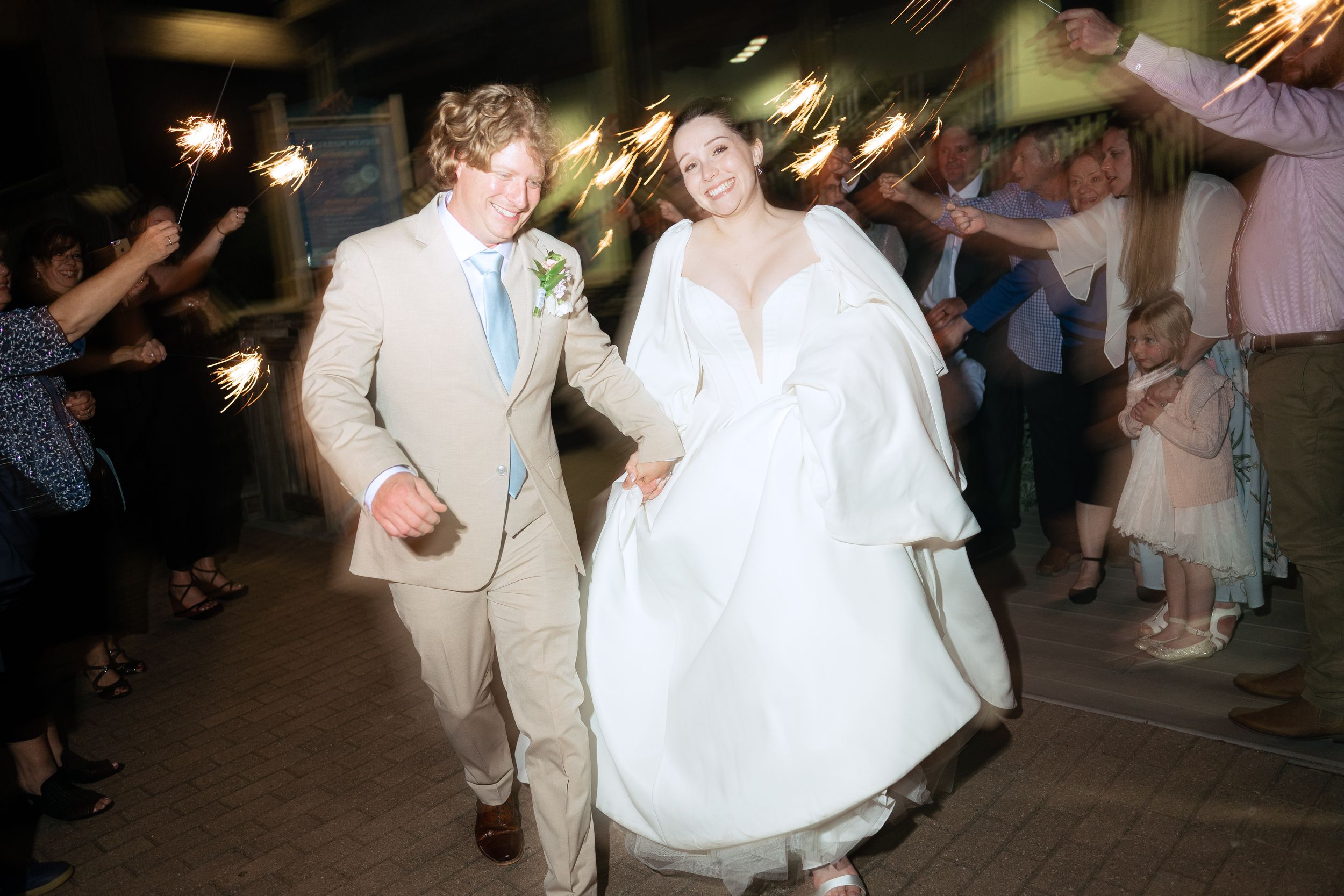 Wedding guests hold sparklers during nighttime celebration creating trails of light in the darkness.