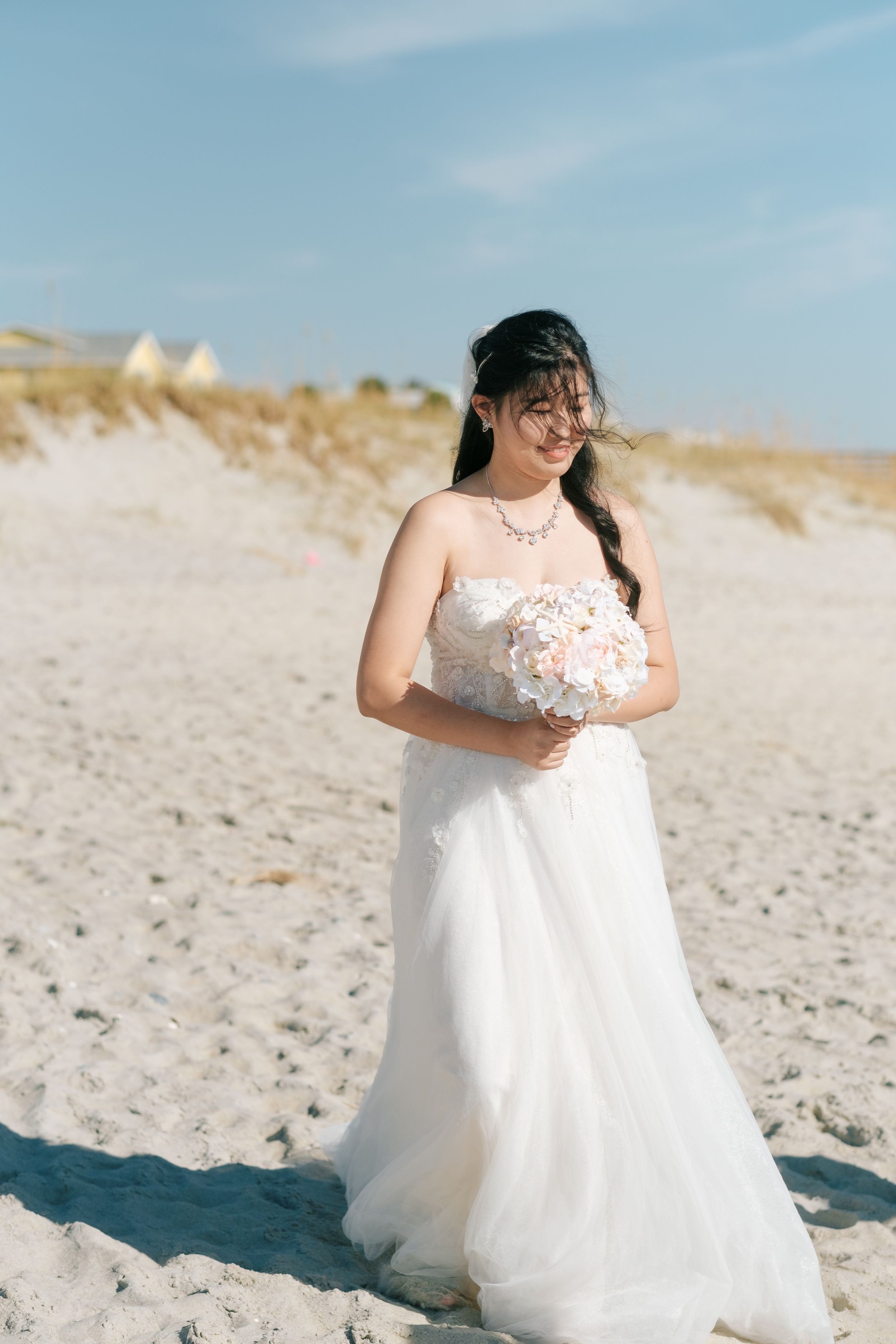 Bride in a flowing white wedding dress poses gracefully on a sunny beach.