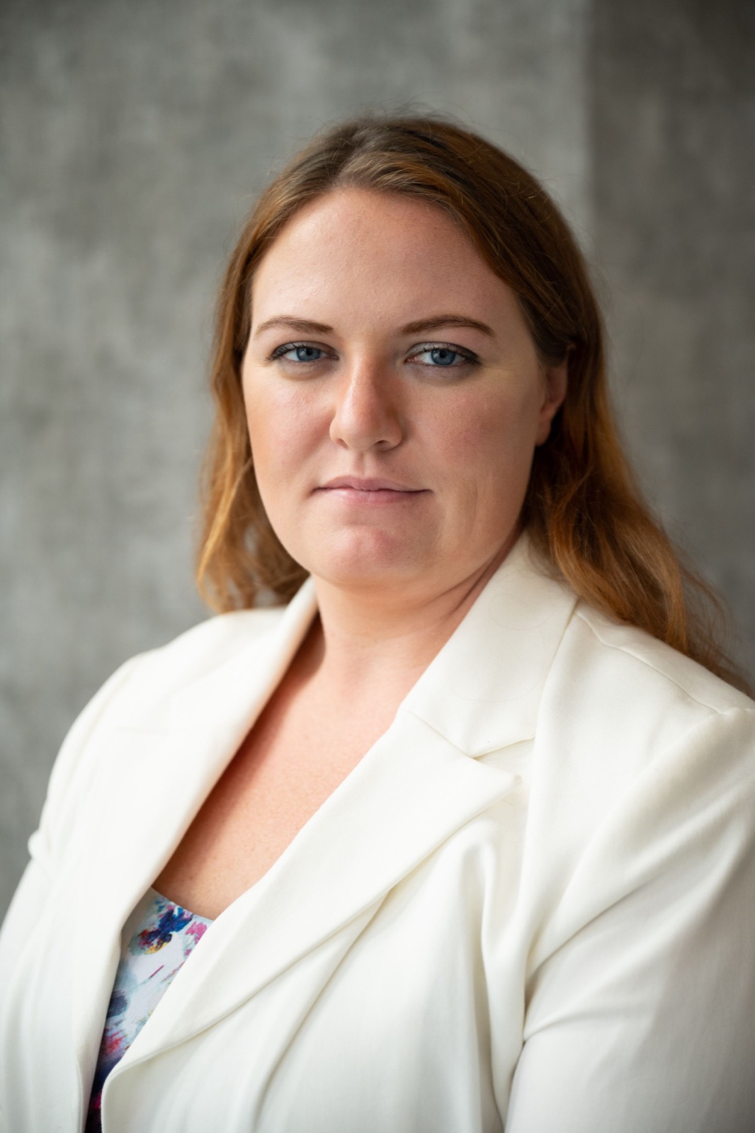 Professional headshot of a person wearing a white blazer against a gray background.