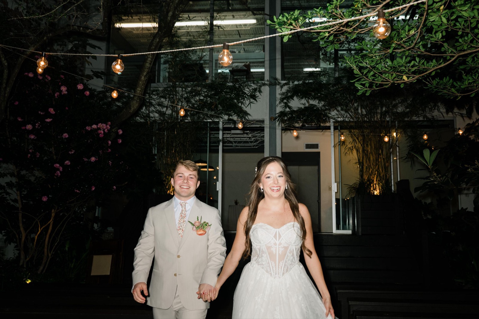 Newlyweds exiting their wedding venue at night under romantic string lights in the garden.