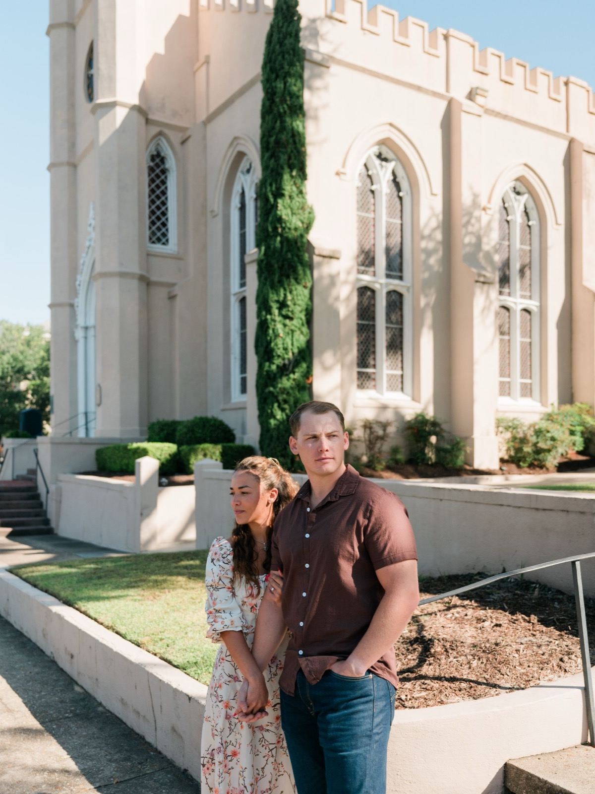 A couple standing together outside a Gothic Revival style church with white walls and arched windows.