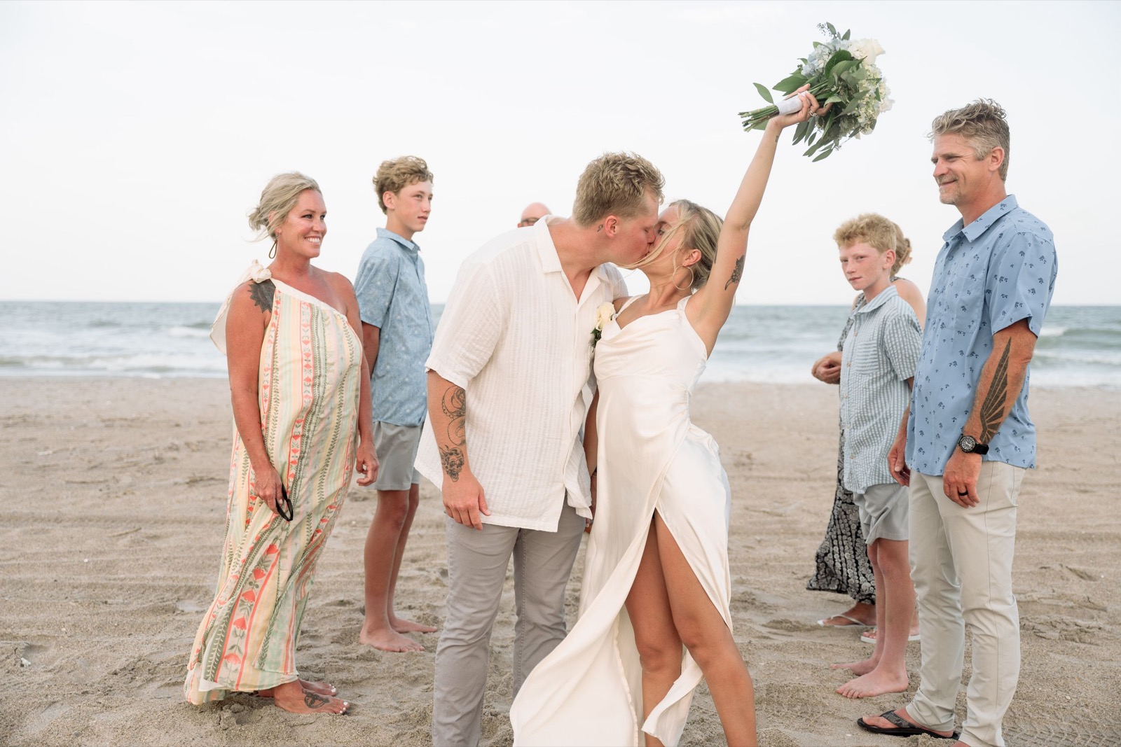 A joyful beach wedding celebration with wedding party dressed in casual attire by the sea.