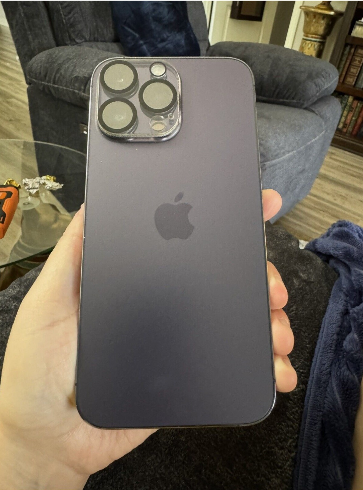 Black iPhone 13 Pro with triple camera setup held against gray couch background.