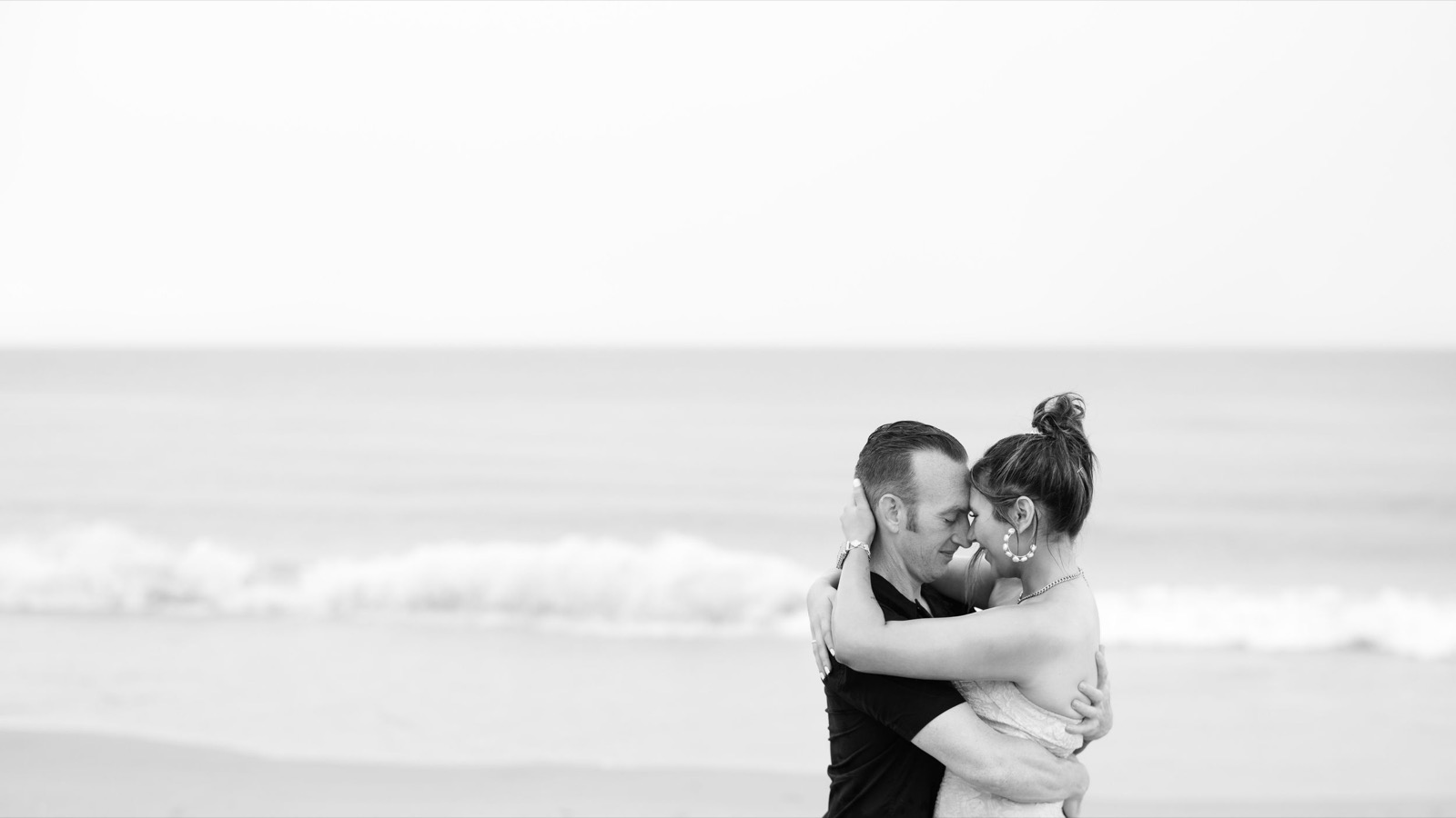 A romantic beach embrace at sunset captured in black and white photography.