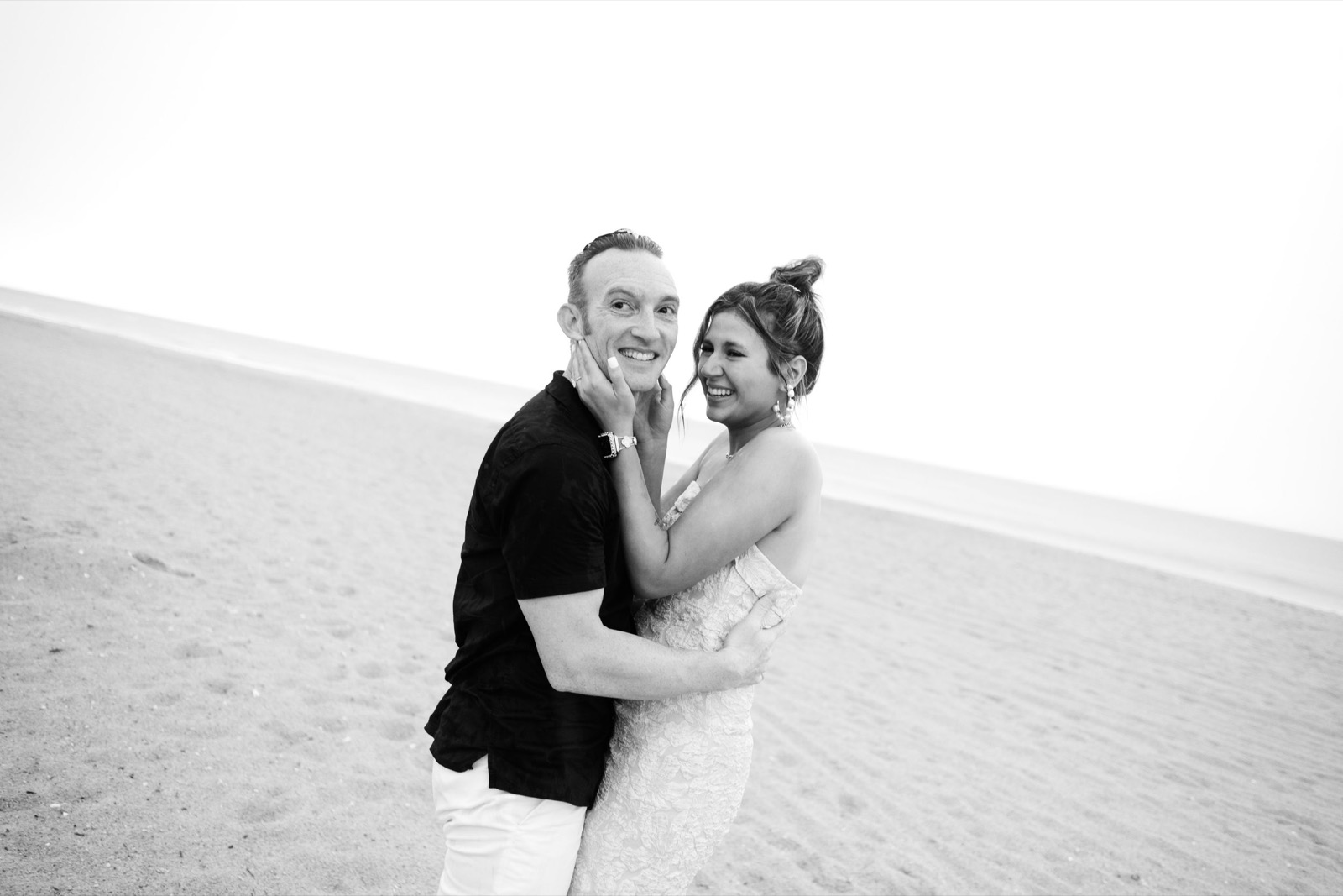 A joyful couple embracing on a sandy beach in black and white.