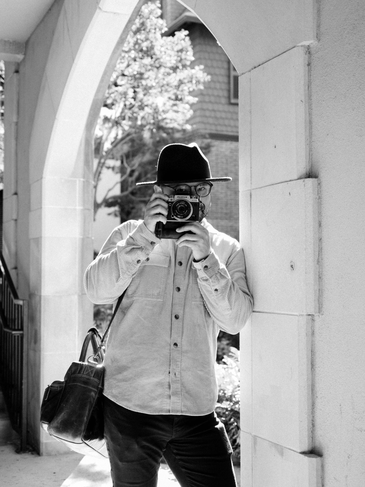 Black and white photo of photographer taking self portrait in an archway.