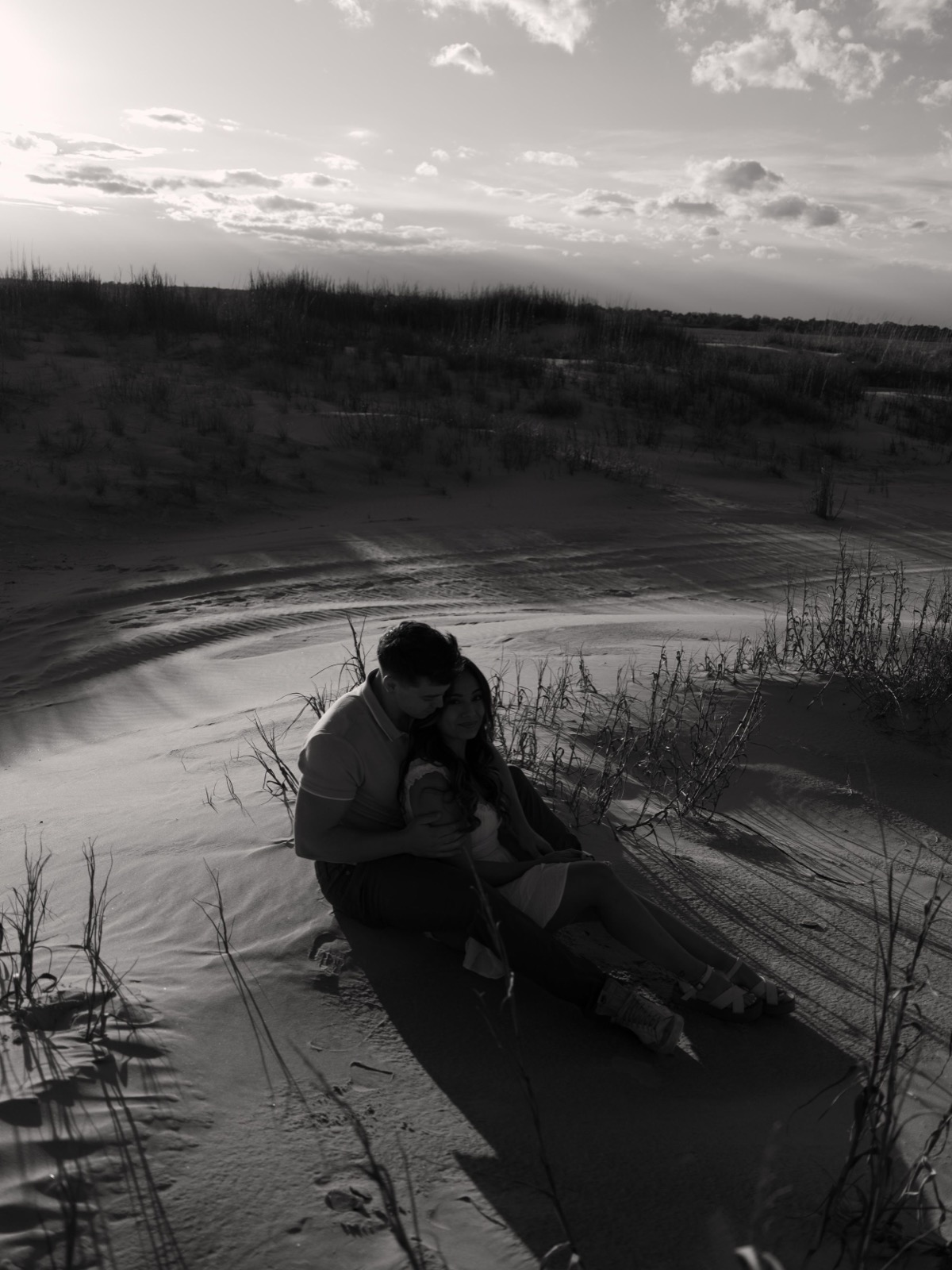 Silhouette of a person sitting by a lake during sunset at dusk in a moody black and white scene.