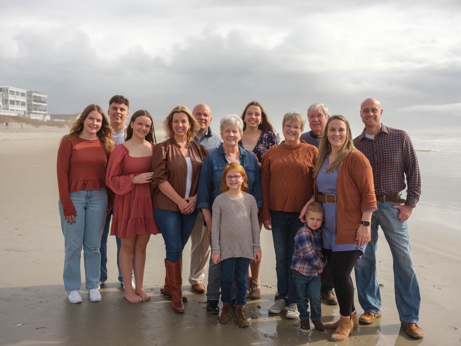 Extended family posing together for a group photo on a cloudy beach.