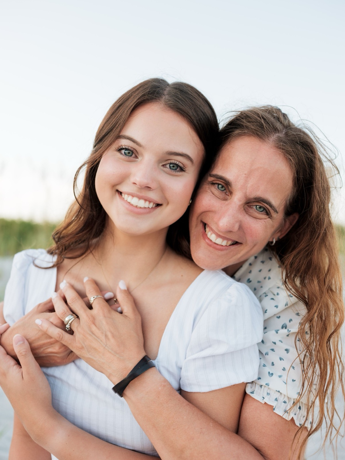 A close-up portrait of two people embracing and smiling at the camera outdoors.