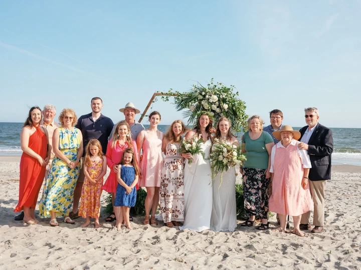 Wedding party and family gathered on the beach with the ocean behind them