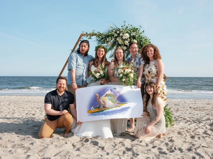 Small wedding group holding an illustrated sign on the beach