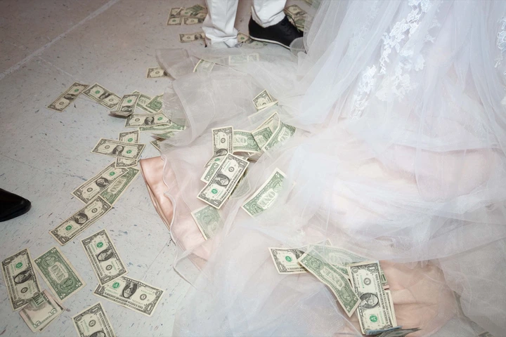 Cash money scattered on the floor around the hem of a white wedding dress.