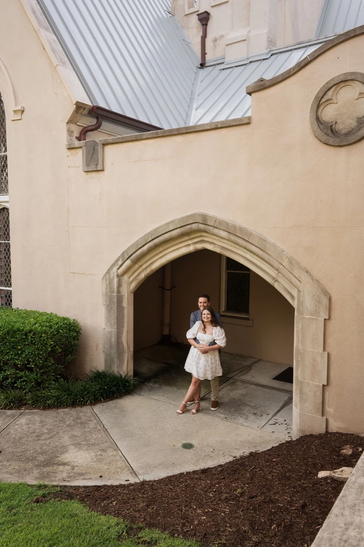 A white stone archway entrance to a church or historic building with landscaped grounds.
