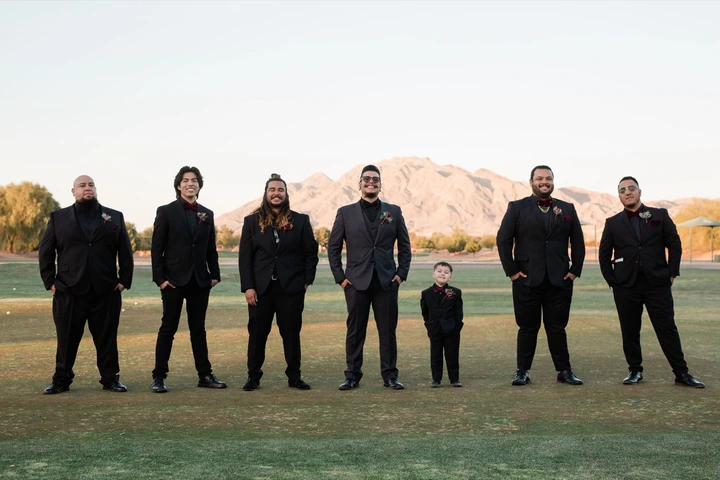 A group of people in formal black attire standing on grass with mountains in background.
