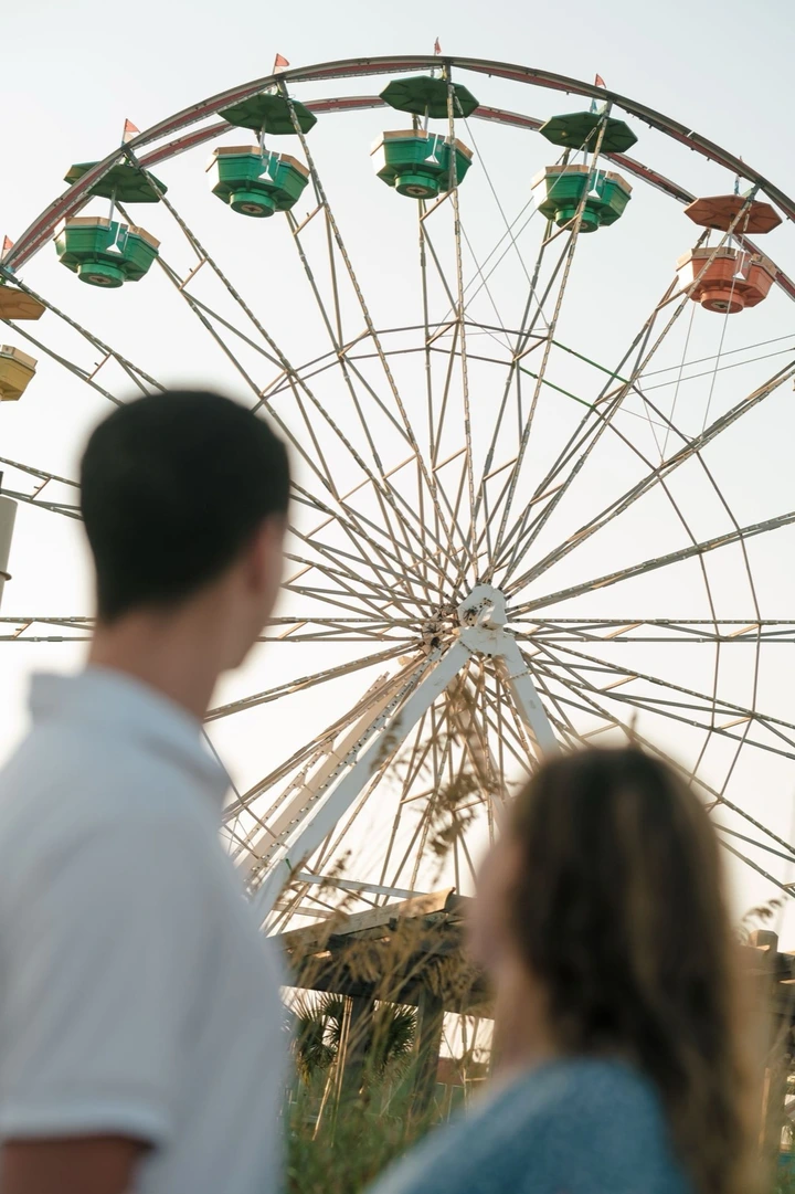 Silhouettes of people standing against a sunset sky with a Ferris wheel in the background.