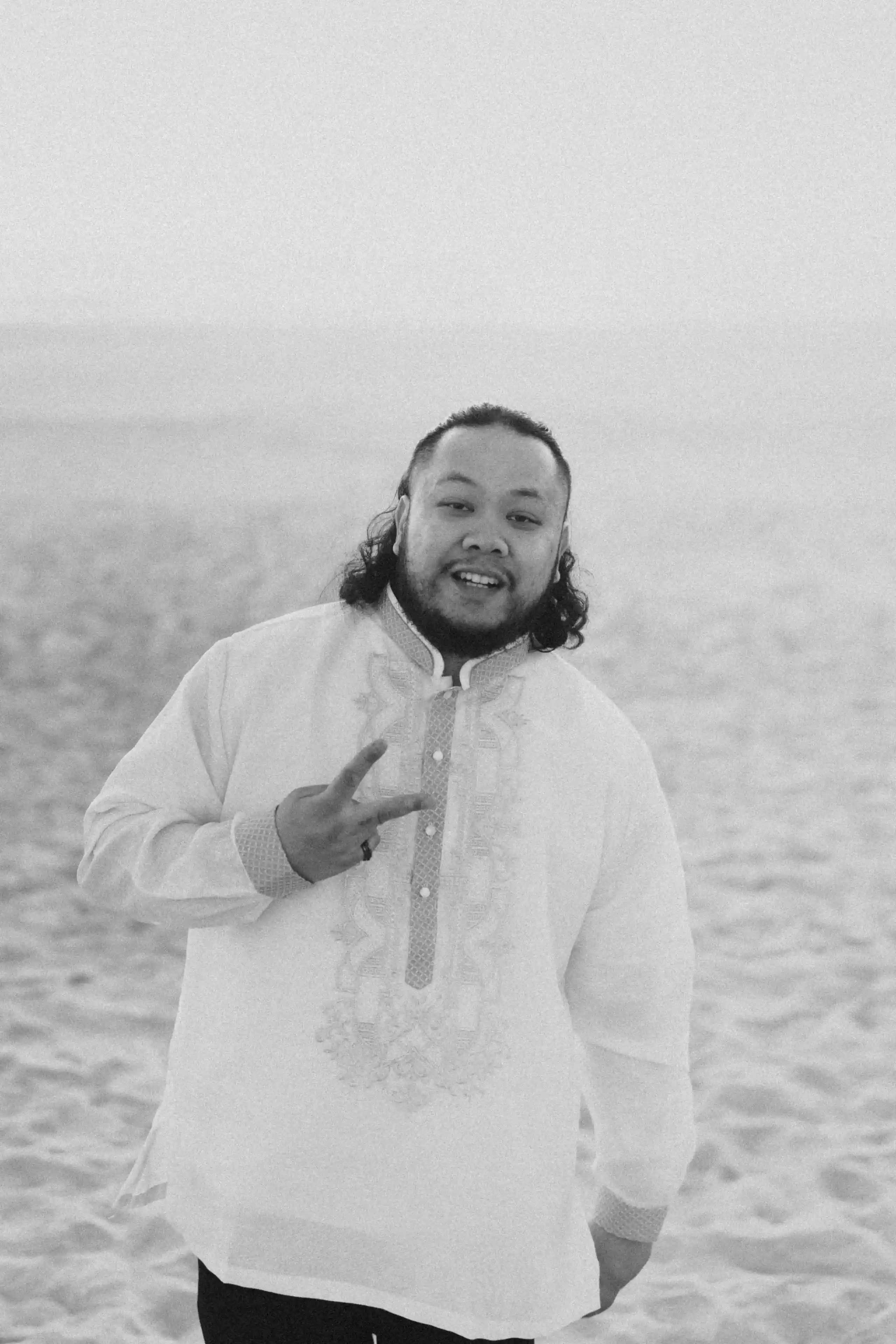 Two friends in casual wear standing together and smiling on a beach with a pier behind them.