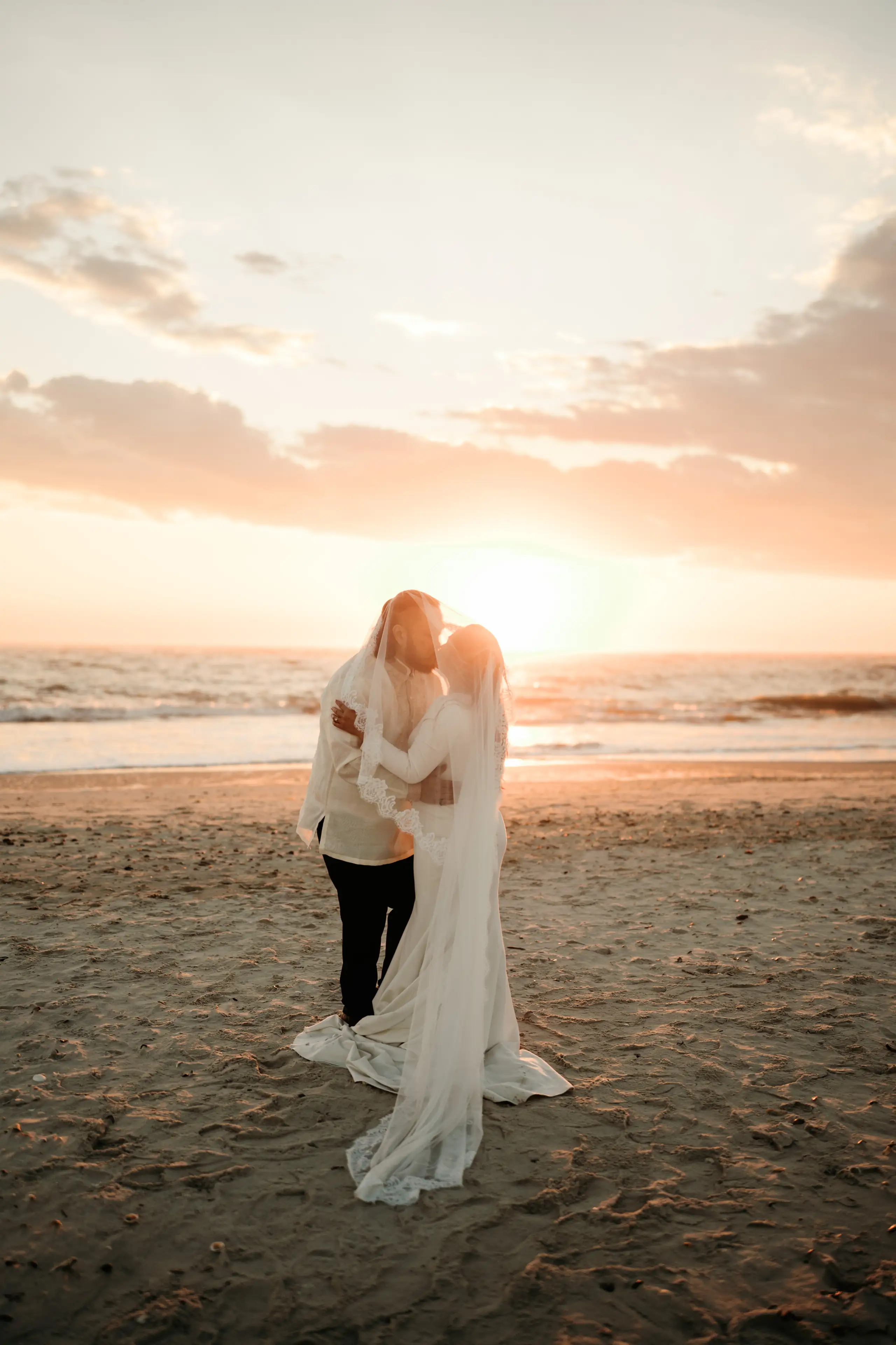 A couple walking along a sandy beach path through sea oats at sunset creating a romantic silhouette.